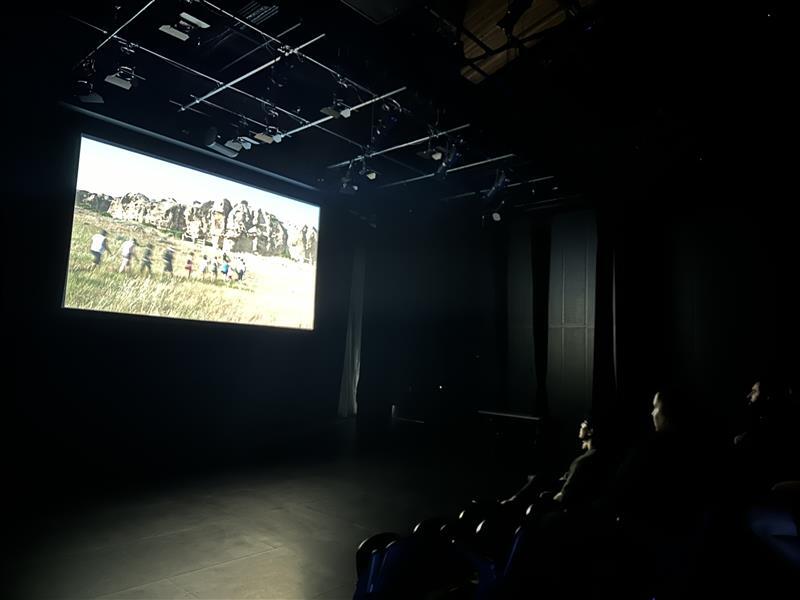 A dark theatre shows an image on a projector with folks in the audience watching