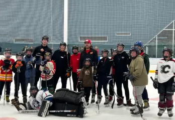Group of youth wearing hockey gear on the ice smiling with Calgary Flames Forward, Ryan Lomberg