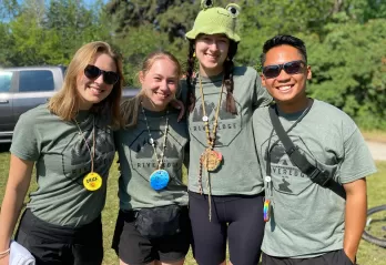Four camp counselors stand with their arms across each others shoulders smiling. 