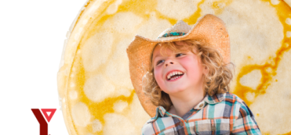 A little boy with a straw cowboy hat and blonde curly hair sits in front of a giant pancake