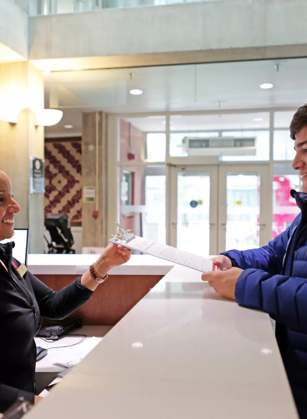 A photo of a young man handing a form to a YMCA employee at the front desk.