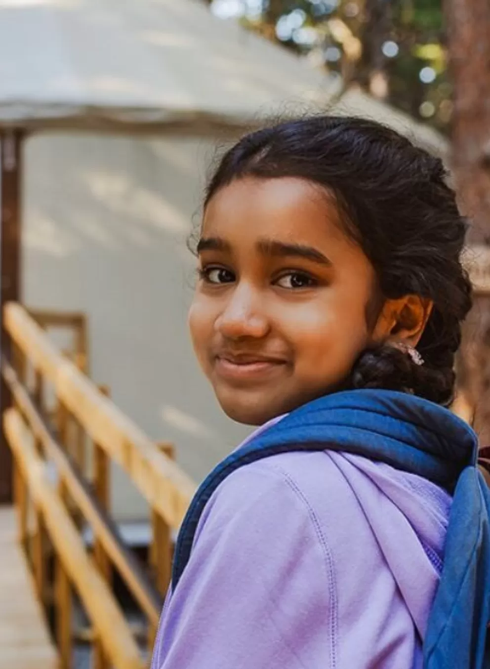 Two girls smiling in front of a yurt at camp in sunlight.