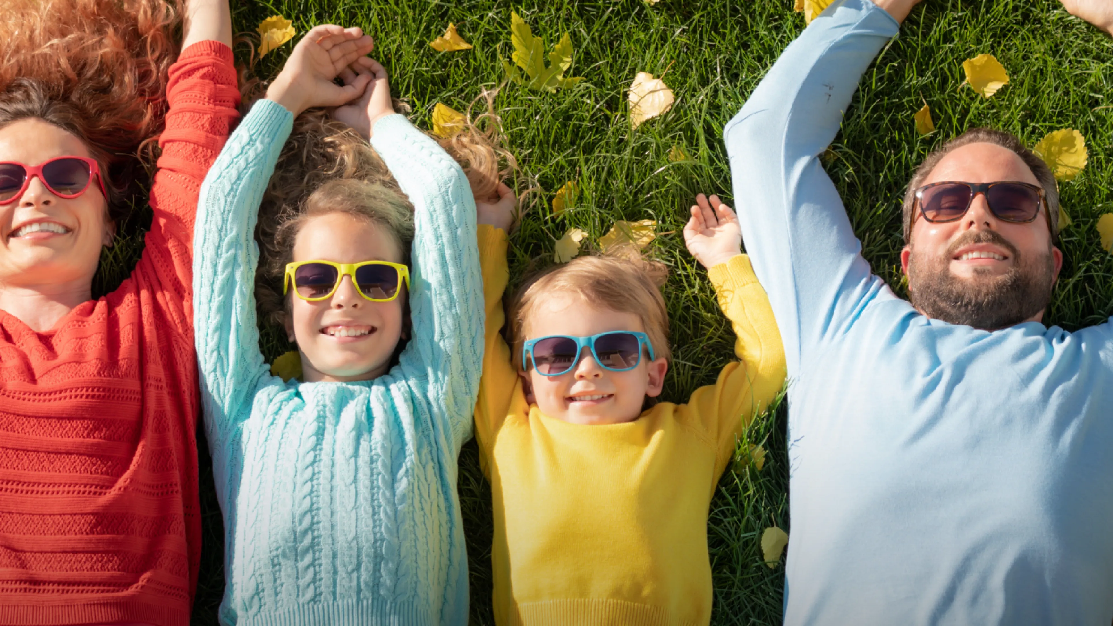 A family lays in the summery grass with matching sunglasses and smiles