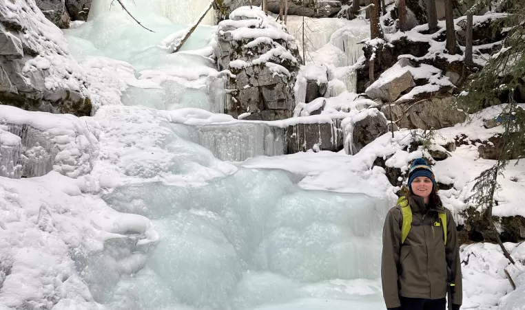 YMCA Staff member Kyla stands next to a frozen waterfall on a winter hike