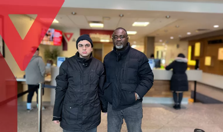 Two gentlemen stand in front of the Member Services desk at Saddletowne YMCA, both wearing black jackets and looking at the camera.