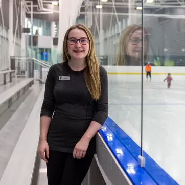 A young woman smiles while leaning against the glass of an ice rink at YMCA Calgary