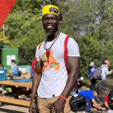 Sam Obadero stands in the sun at Camp Riveredge YMCA, smiling and donning his camera, which he can often be seen with accompanying the smile on his face.