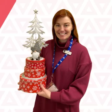 Lisa Rushton poses with the YMCA Calgary holiday gnome in front of a graphic background of YMCA triangles
