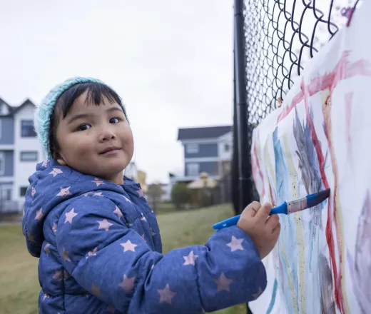 child standing in front of fence painting