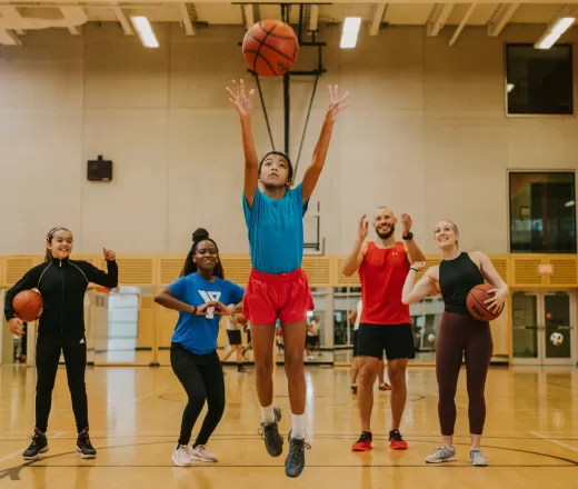 A group of people playing basketball. A girl is taking a shot at the basket.