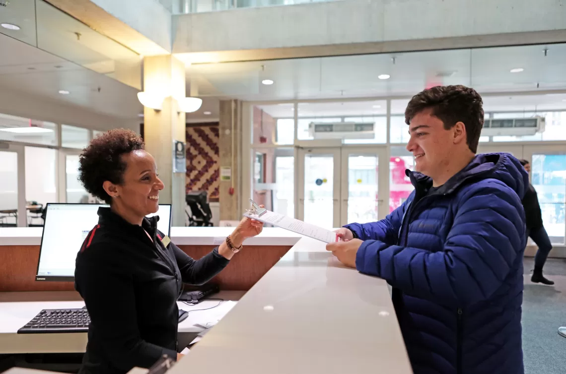 A photo of a young man handing a form to a YMCA employee at the front desk.
