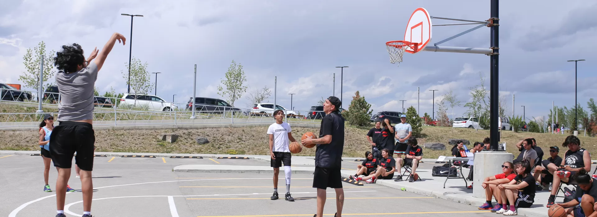 Youth in grey shirt throwing 3 point shot at outside basketball court