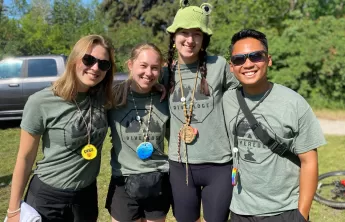 Four camp counselors stand with their arms across each others shoulders smiling. 