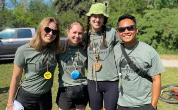 Four camp counselors stand with their arms across each others shoulders smiling. 